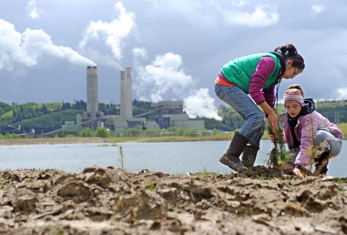 With the TransAlta steam plant billowing in the background, Chehalis Middle School sixth graders Ana Manco and Jessica McKay, left to right, plant a tree Thursday at the company's defunct strip mine site, which is in the process of being reclaimed.